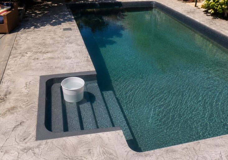 White bucket filled with pool water sitting fully on submerged pool steps for a bucket test.
